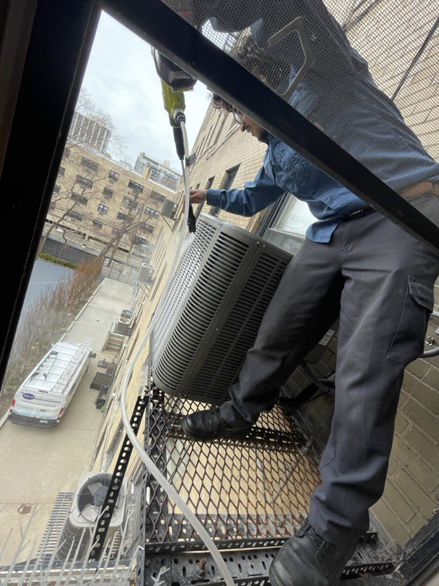 An HVAC technician from Deljo Heating, Cooling & Plumbing servicing an outdoor AC unit on a fire escape in Chicago, IL.