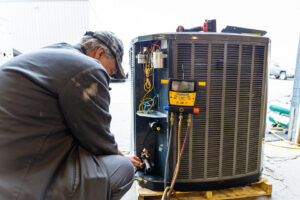 An HVAC technician from DFH Company Heating and Air Conditioning servicing an outdoor AC unit with gauges in Louisville, KY.