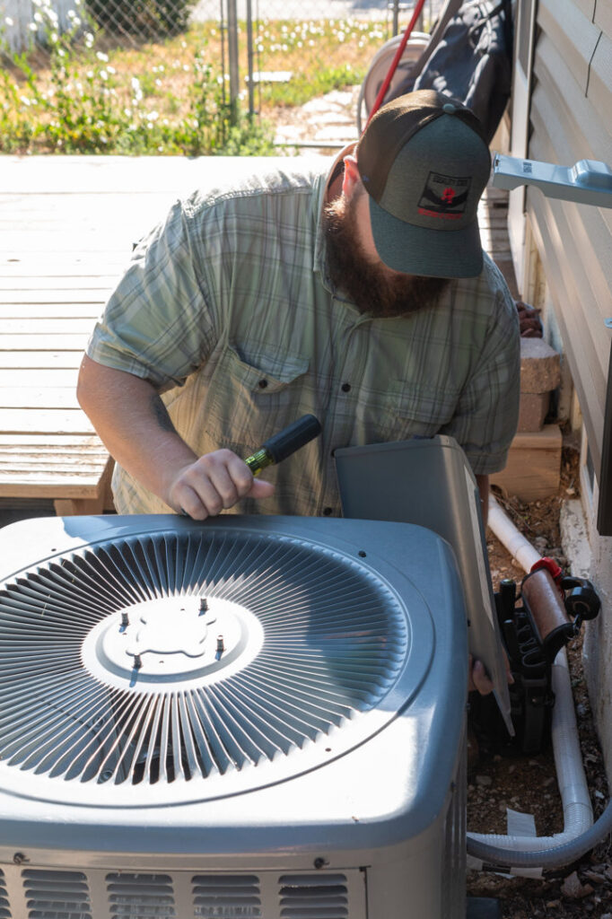 An HVAC technician servicing an outdoor air conditioning unit with tools for Equality State Heating & Cooling in Casper, WY.