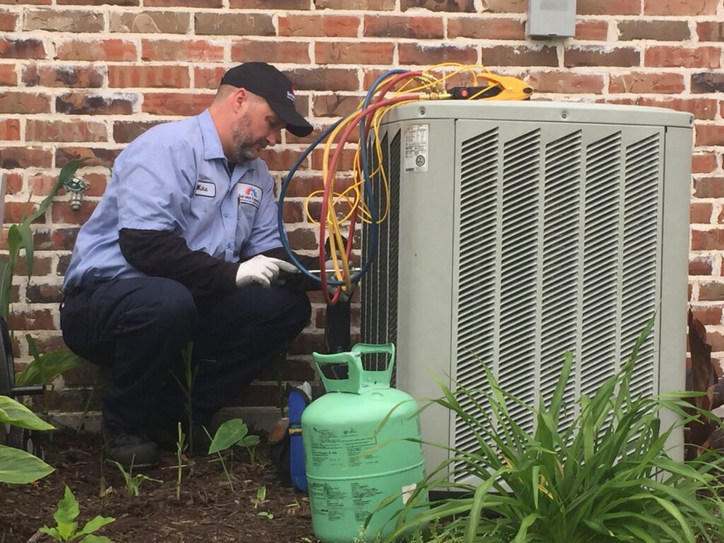 An HVAC technician from Falso Service Experts servicing an outdoor AC unit with gauges and a refrigerant tank in East Syracuse, NY.