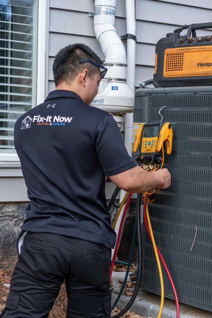 An HVAC technician from Fix It Now Heating and Cooling servicing an outdoor air conditioning unit with gauges in Thornton, CO