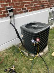 An HVAC technician performing service on an outdoor air conditioning unit with gauges connected for American Team Inc in Warminster, PA