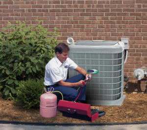 An HVAC technician servicing an outdoor air conditioning unit with gauges and refrigerant at Harry Roberts Plumbing Heating Air Conditioning in Owensboro, KY.