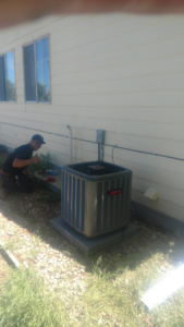 An HVAC technician from Home and Property Services LLC servicing an outdoor air conditioning unit in Aurora, CO.