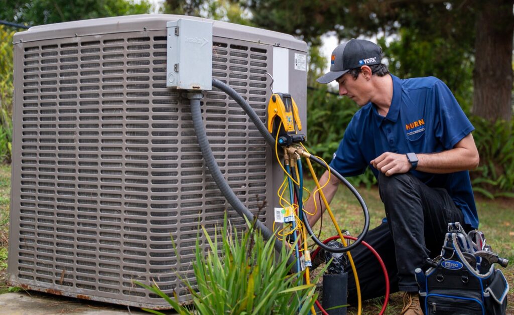 An HVAC technician servicing an outdoor AC unit with gauges for Hurn Mechanical Heating & Cooling in El Cajon, CA.