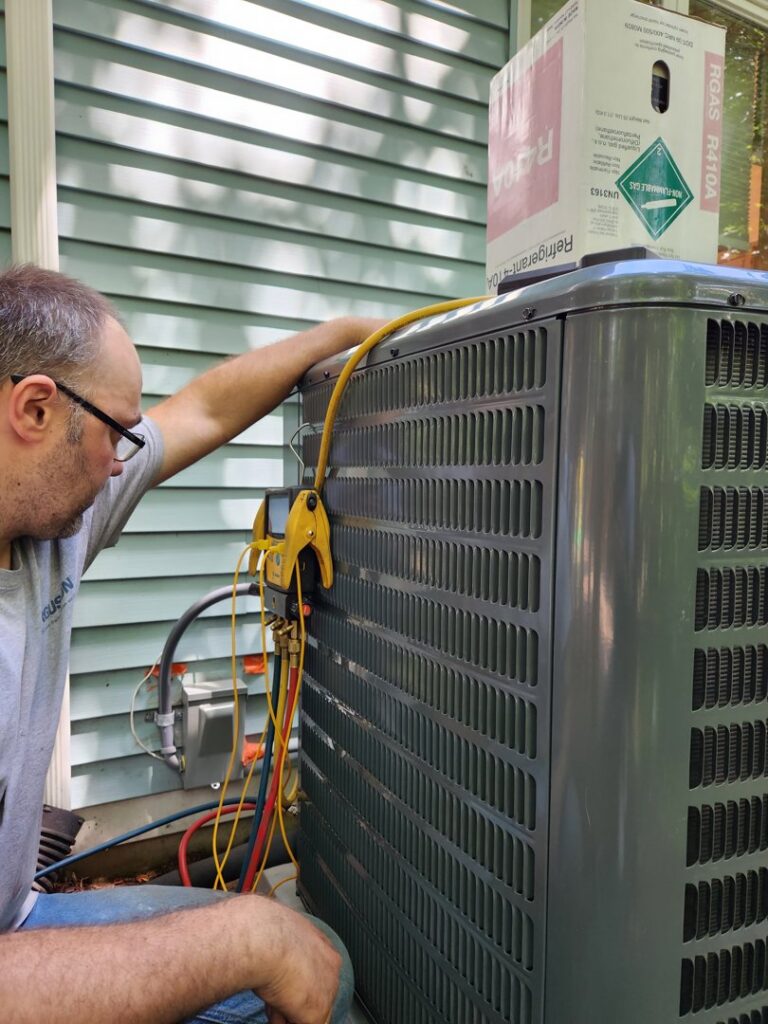 An HVAC technician connecting gauges to an outdoor air conditioning unit for service by HVAC Fellows in Boston, MA.