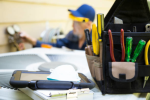 An HVAC technician servicing an outdoor air conditioning unit, with tools in the foreground, by Joe Logan HVAC in Dayton, OH.