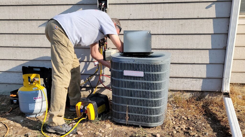 An HVAC technician from Kraemer Mechanical servicing an outdoor AC unit with tools and tanks in Broomfield, CO.