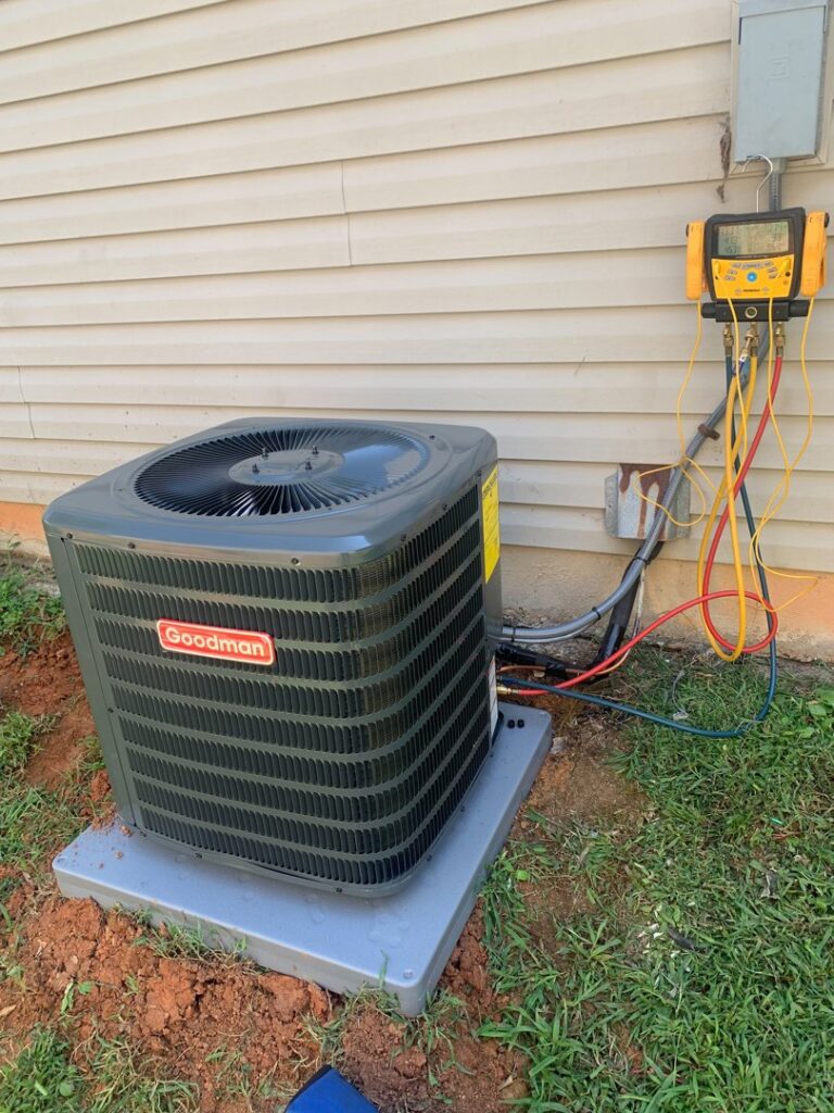 An HVAC technician servicing a Goodman outdoor AC unit with gauges connected by MTZ Heating and Air Conditioning in Charlotte, NC.