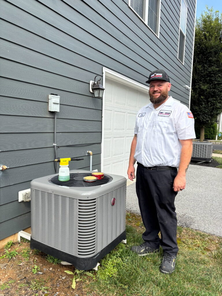 An HVAC technician from One Hour Heating & Air Conditioning of Lancaster, PA, standing next to an outdoor AC unit with cleaning supplies.