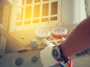 An HVAC technician servicing an outdoor air conditioning unit with manifold gauges for Reliance Home Comfort in Hampton, VA.