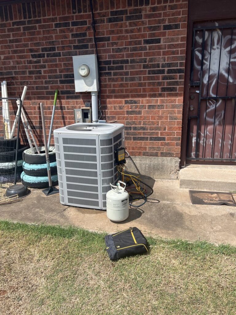 An HVAC technician servicing an outdoor AC unit with gauges and a refrigerant tank, performed by Rhino Heating and Air Conditioning LLC in Norman, OK.