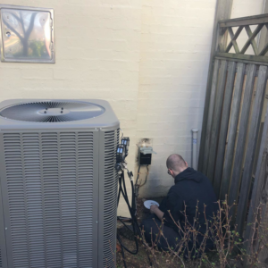 An HVAC technician servicing an outdoor air conditioning unit for SFC Heating and A/C, LLC in Alexandria, VA.