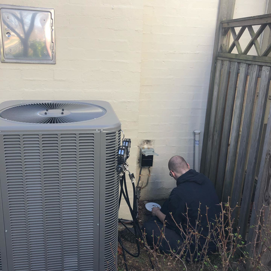An HVAC technician servicing an outdoor air conditioning unit for SFC Heating and A/C, LLC in Alexandria, VA.