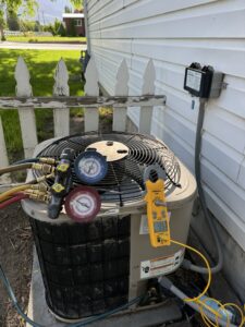 HVAC technician servicing an outdoor AC unit with gauges and amp clamp for diagnostics by EPIC Heating and Air in Loveland, CO