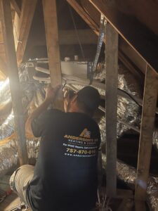 An HVAC technician servicing an air handler unit in an attic for Anderson's Air in Newport News, VA
