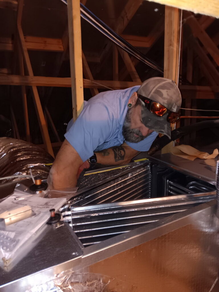 An HVAC technician servicing an air handler unit in an attic for Bishop Air Service in Henderson, NV.