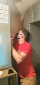 An HVAC technician wearing a mask performing service on an indoor air handler unit for Bama Air Systems in Cullman, AL.