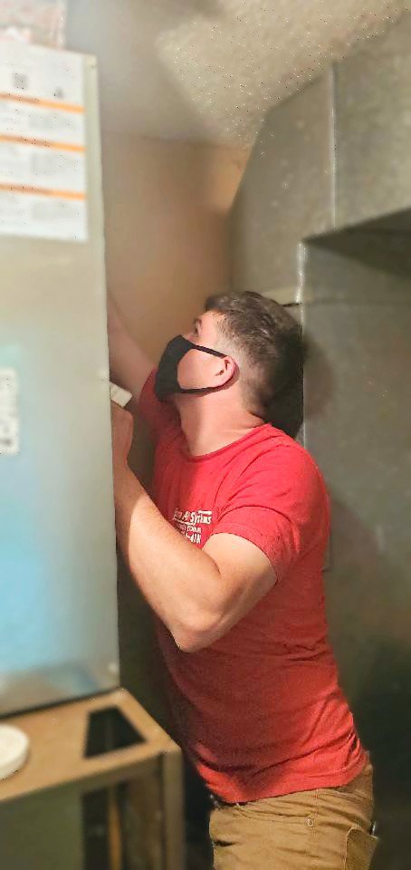 An HVAC technician wearing a mask performing service on an indoor air handler unit for Bama Air Systems in Cullman, AL.