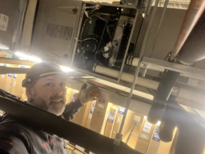 An HVAC technician from Kusi.aat' Kaa' Refrigeration servicing an overhead air handler unit in Homer, AK.