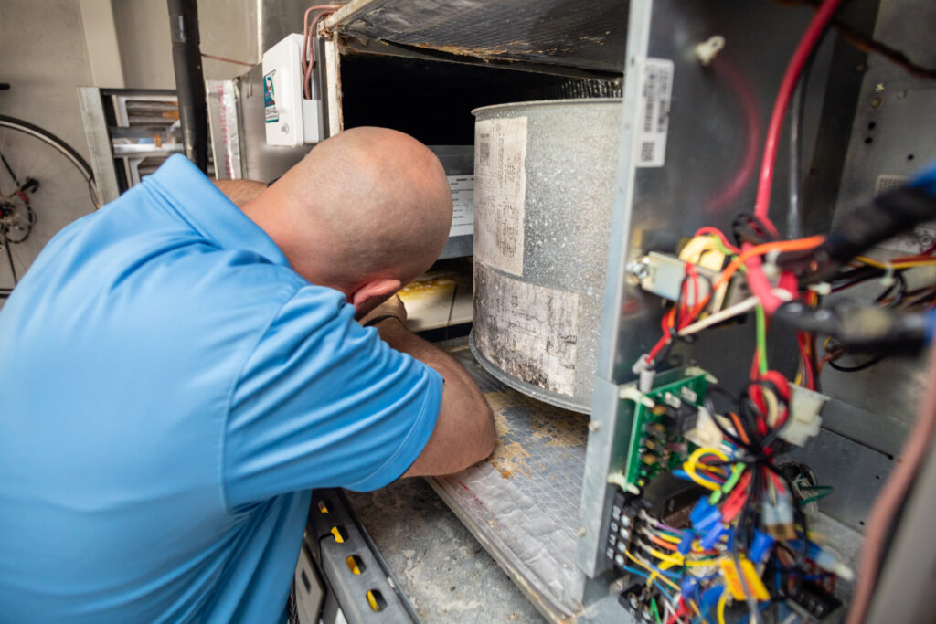 An HVAC technician servicing an indoor air handler unit with exposed wiring for Surfside Heating & Cooling in Cape Coral, FL.