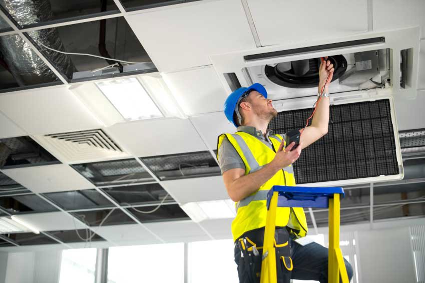 An HVAC technician servicing a ceiling-mounted unit with a multimeter for Glendale HVAC in Glendale, AZ