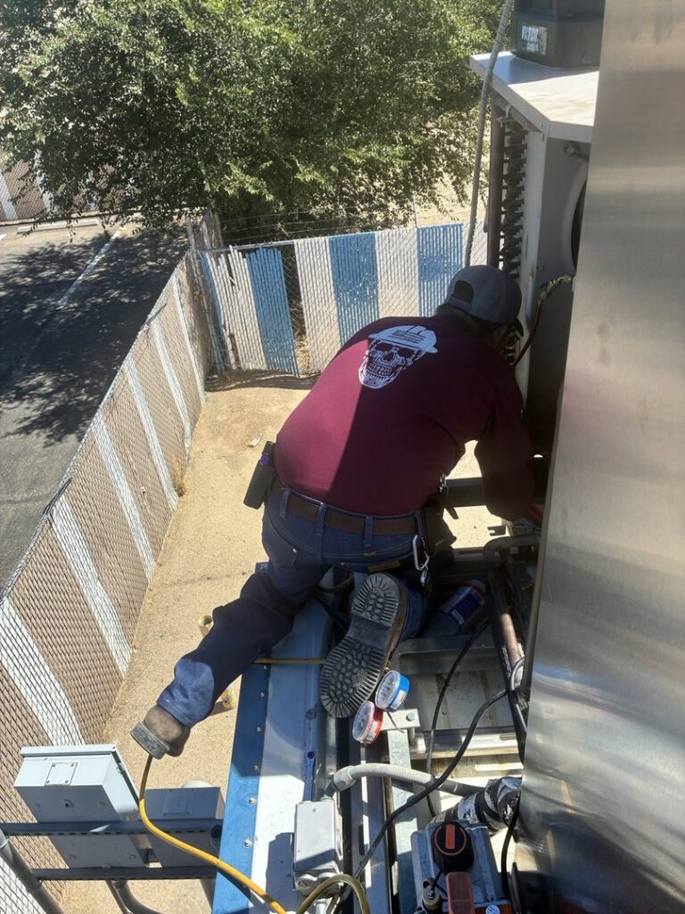 An HVAC technician performing service on a commercial outdoor condenser unit for Four Corners Service Co. in Farmington, NM.