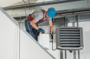 An HVAC technician in a hard hat servicing an overhead commercial heating unit, performed by Jons-Air in Carmel, IN.