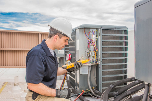 An HVAC technician in a hard hat servicing a commercial rooftop unit for General Air Conditioning Service Corp in Greenville, SC.