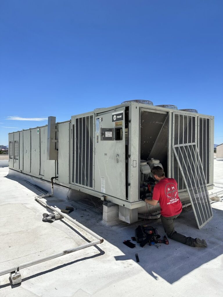 An HVAC technician servicing a large commercial rooftop unit for Rogue Mechanical in Las Vegas, NV.