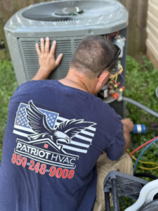 A Patriot HVAC Services technician in Richmond, KY, servicing an outdoor air conditioning condenser unit.