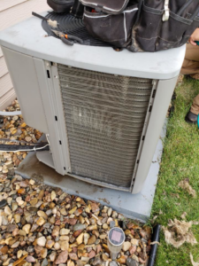 An HVAC technician servicing a residential air conditioning unit with dirty coils at a home in Bismarck, ND, by Schaff Heating and Air, LLC.
