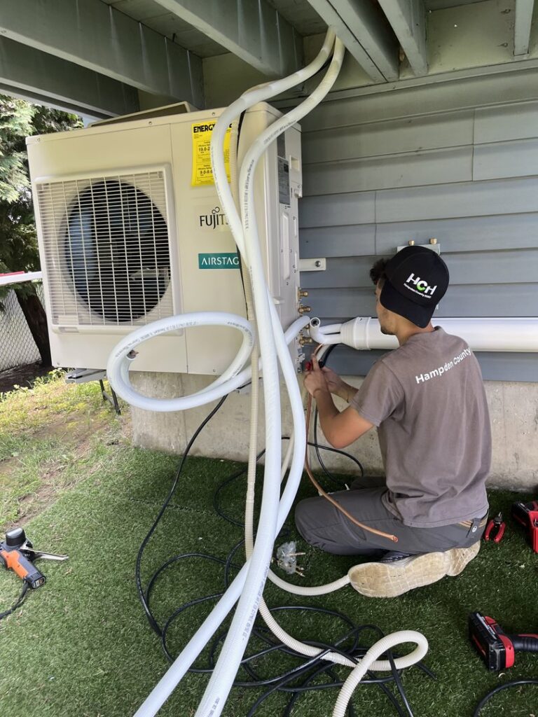 An HVAC technician servicing an outdoor Fujitsu mini-split unit for Hampden County HVAC Inc. in Indian Orchard, MA