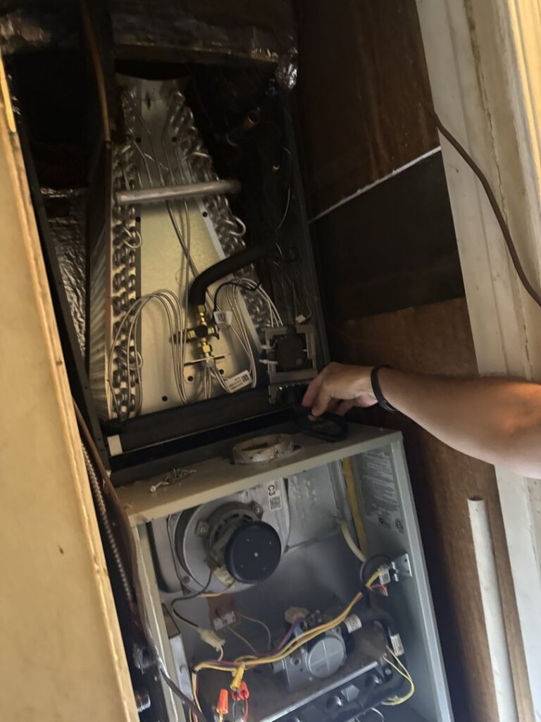 An HVAC technician servicing the internal components of a furnace unit for AirTech Solutions LLC in Broken Arrow, OK.