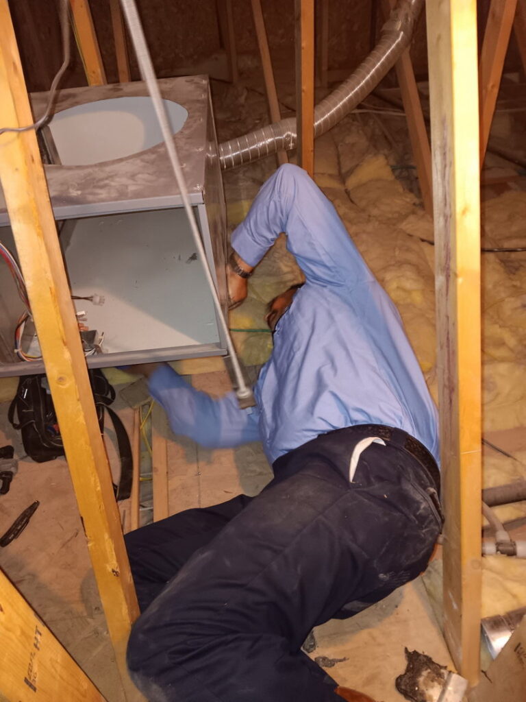 An HVAC technician servicing a furnace or air handler unit in an attic for Bishop Air Service in Henderson, NV.