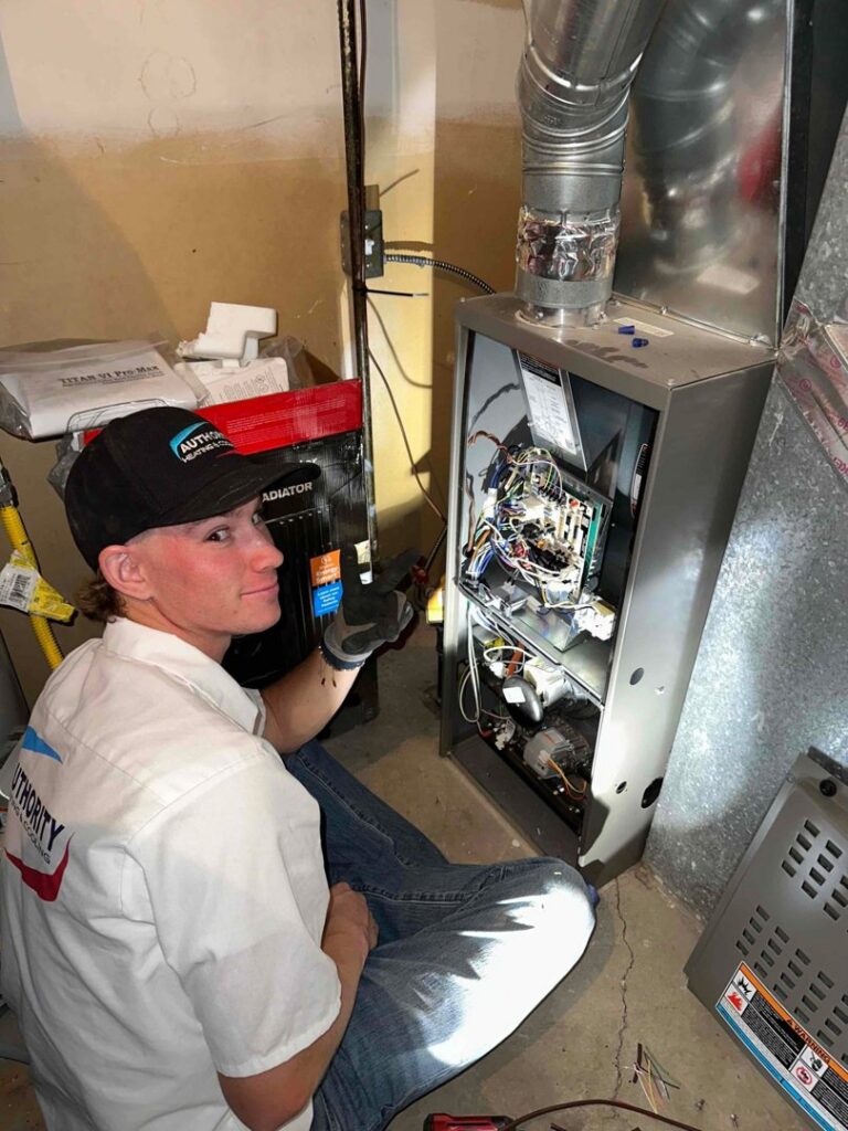 An HVAC technician from Authority Heating & Cooling servicing an open furnace unit in a residential basement in Orem, UT.