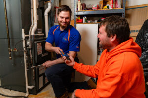 An HVAC technician from Swiss Air Heating & Cooling servicing a furnace while interacting with a customer in O'Fallon, MO.