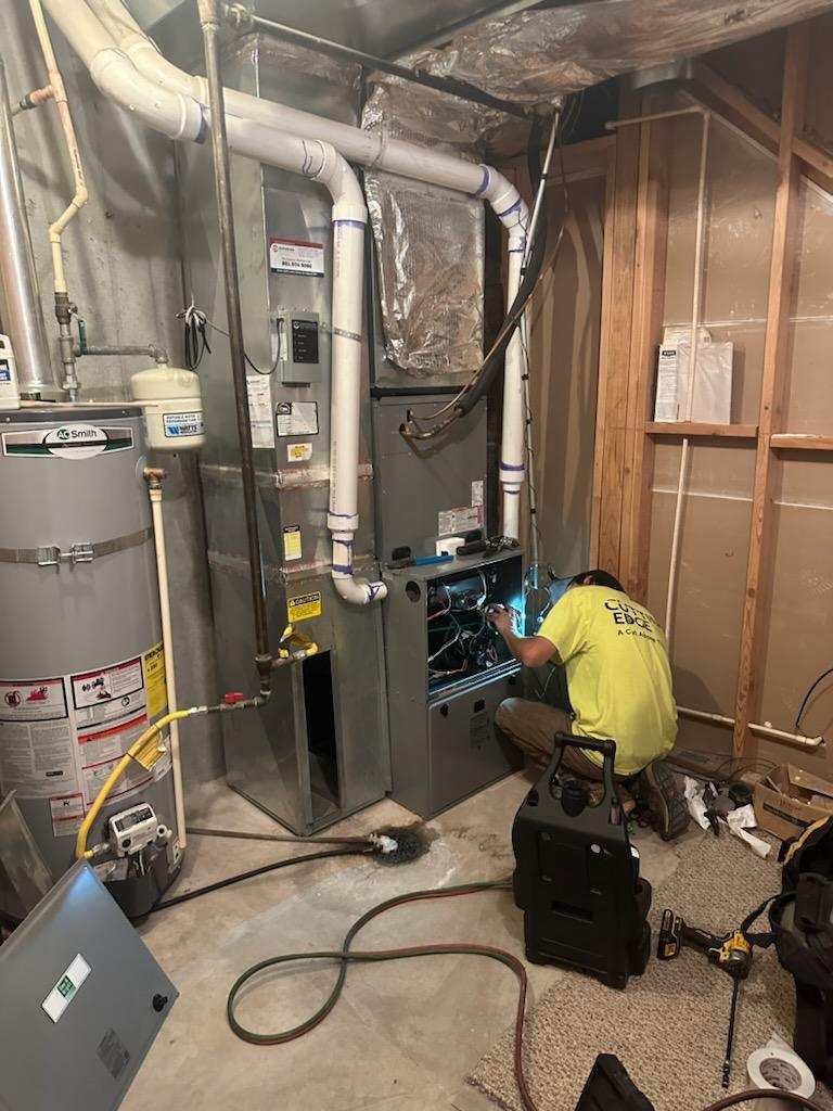 An HVAC technician servicing a furnace unit in a basement for Cutting Edge HVAC LLC in Orem, UT.