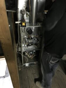 An HVAC technician servicing an open furnace unit in a tight space for Epic Heating & Cooling in Wichita, KS.
