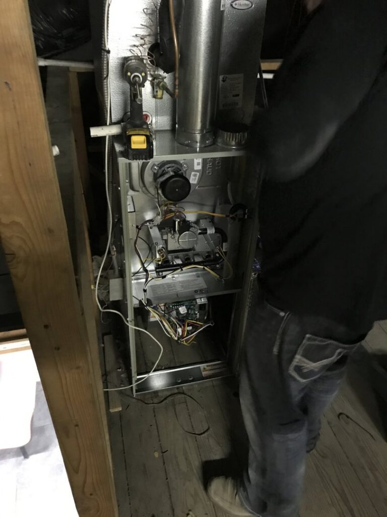 An HVAC technician servicing an open furnace unit in a tight space for Epic Heating & Cooling in Wichita, KS.