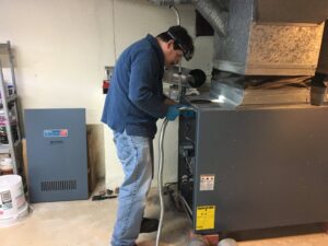 An HVAC technician servicing a furnace or boiler unit in a basement for Garrison City HVACR in Dover, NH