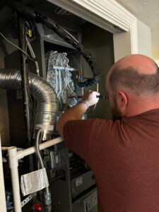 An HVAC technician servicing an indoor furnace or air handler unit for Goodie Heating & Air in Sandy, UT.