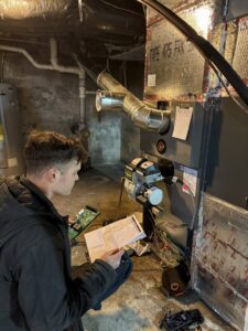 An HVAC technician from JK Mechanical servicing a furnace or boiler unit in a residential basement in Willow Street, PA.