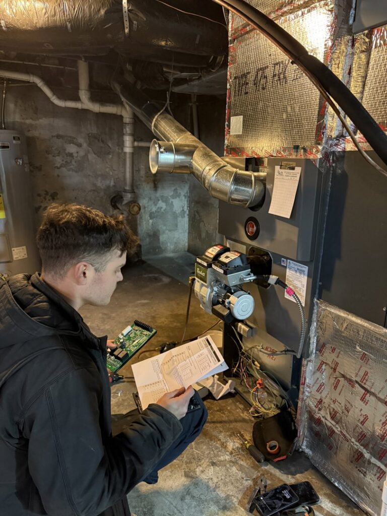 An HVAC technician from JK Mechanical servicing a furnace or boiler unit in a residential basement in Willow Street, PA.