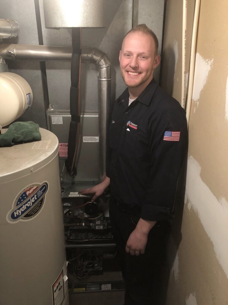 An HVAC technician smiling while servicing an open furnace unit for Peterson Heating & Cooling in Mound City, KS.
