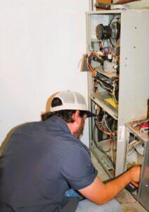 An HVAC technician performing maintenance and repair on a furnace unit for Stoker Mechanical Heating & Air Conditioning in Lawrence, KS.