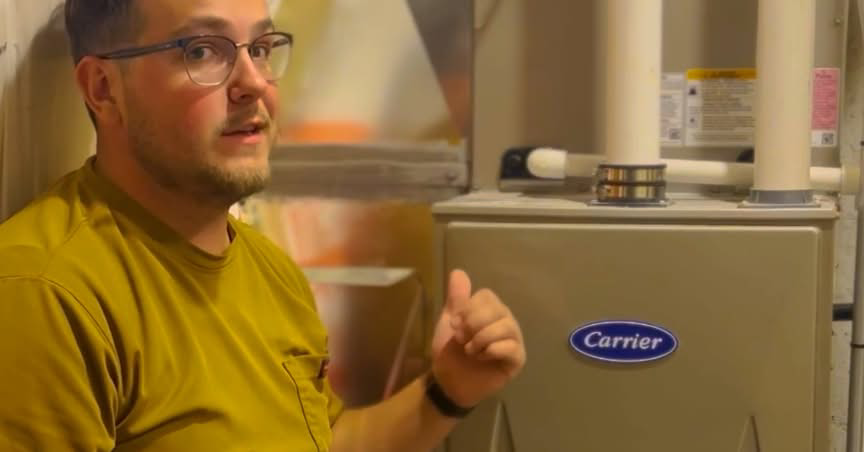 An HVAC technician from Trade Standard HVAC explaining or servicing a Carrier furnace unit in Magna, UT.