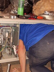 An Air Specialty Heating & Air Conditioning technician servicing an indoor furnace unit in Norfolk, VA.