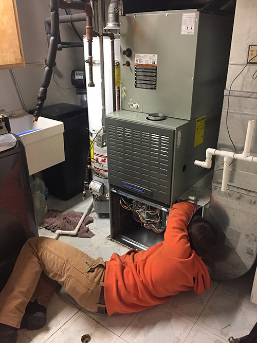 An HVAC technician servicing an indoor furnace unit on the floor for Fellowship Heating and Cooling in Indianapolis, IN.