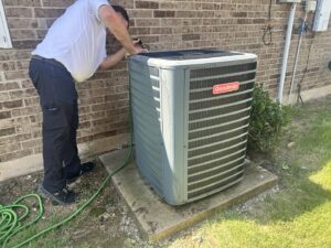 An HVAC technician servicing an outdoor Goodman AC unit at a residential property for One Hour Air Conditioning & Heating of Fort Worth, TX.